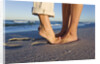 Feet of couple hugging on beach by Anonymous