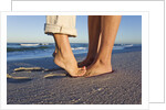 Feet of couple hugging on beach by Anonymous