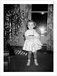 A little girl stands by the Christmas tree clutching her doll, ca. 1955 by Anonymous
