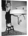 A young girl brushes her teeth at the sink, ca. 1955 by Anonymous