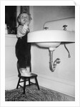 A young girl brushes her teeth at the sink, ca. 1955 by Anonymous