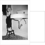 A young girl brushes her teeth at the sink, ca. 1955 by Anonymous