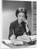Brunette business woman sitting desk talking telephone writing note on calendar by Anonymous