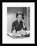 Brunette business woman sitting desk talking telephone writing note on calendar by Anonymous