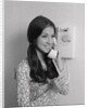 Smiling teenage girl talking on rotary wall telephone by Anonymous