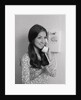 Smiling teenage girl talking on rotary wall telephone by Anonymous