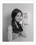 Smiling teenage girl talking on rotary wall telephone by Anonymous