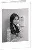 Smiling teenage girl talking on rotary wall telephone by Anonymous