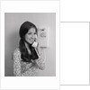 Smiling teenage girl talking on rotary wall telephone by Anonymous