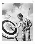 Boy jeans striped t-shirt holding bow & pulling arrow out of target bull's-eye by Anonymous