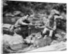 Couple having picnic sitting on rocks by stream man pouring drink for woman from thermos by Anonymous