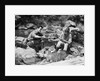 Couple having picnic sitting on rocks by stream man pouring drink for woman from thermos by Anonymous