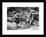 Couple having picnic sitting on rocks by stream man pouring drink for woman from thermos by Anonymous