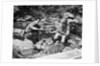 Couple having picnic sitting on rocks by stream man pouring drink for woman from thermos by Anonymous