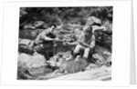 Couple having picnic sitting on rocks by stream man pouring drink for woman from thermos by Anonymous