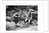 Couple having picnic sitting on rocks by stream man pouring drink for woman from thermos by Anonymous