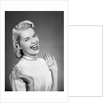 Woman wearing pearls smiling with hands up thumbs tucked under arm by Anonymous