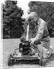 Elderly man in yard kneeling down to fix lawnmower by Anonymous