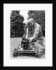 Elderly man in yard kneeling down to fix lawnmower by Anonymous