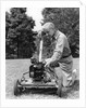 Elderly man in yard kneeling down to fix lawnmower by Anonymous