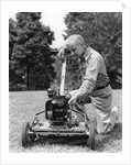Elderly man in yard kneeling down to fix lawnmower by Anonymous