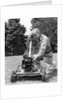 Elderly man in yard kneeling down to fix lawnmower by Anonymous