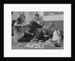 Family mother kids playing board game living room floor father reading newspaper by Anonymous