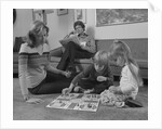 Family mother kids playing board game living room floor father reading newspaper by Anonymous