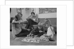 Family mother kids playing board game living room floor father reading newspaper by Anonymous