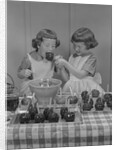 Two twin girls eating making candy apples in kitchen by Anonymous