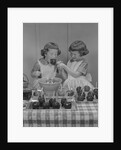 Two twin girls eating making candy apples in kitchen by Anonymous