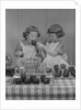 Two twin girls eating making candy apples in kitchen by Anonymous