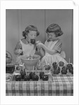 Two twin girls eating making candy apples in kitchen by Anonymous