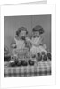 Two twin girls eating making candy apples in kitchen by Anonymous
