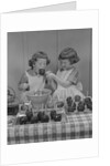 Two twin girls eating making candy apples in kitchen by Anonymous