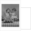 Two twin girls eating making candy apples in kitchen by Anonymous