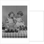 Two twin girls eating making candy apples in kitchen by Anonymous