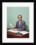 Smiling man at desk holding papers with mortgage officer sign looking at camera by Anonymous