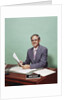 Smiling man at desk holding papers with mortgage officer sign looking at camera by Anonymous