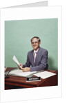 Smiling man at desk holding papers with mortgage officer sign looking at camera by Anonymous