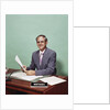 Smiling man at desk holding papers with mortgage officer sign looking at camera by Anonymous