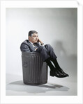 Sad man in business suit sitting in trash garbage can by Anonymous