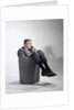 Sad man in business suit sitting in trash garbage can by Anonymous