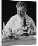 Male scientist wearing white lab coat writing data on clip board holding focus control of microscope by Anonymous
