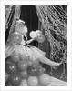 Woman dressed in harlequin costume sitting on stack of balloons by Anonymous