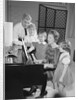 Family standing around piano singing by Anonymous