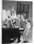 Family standing around piano singing by Anonymous