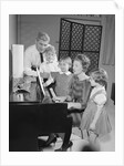 Family standing around piano singing by Anonymous