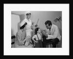Mother sitting watching man pediatric doctor woman nurse checking on smiling little girl patient by Anonymous