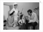 Mother sitting watching man pediatric doctor woman nurse checking on smiling little girl patient by Anonymous